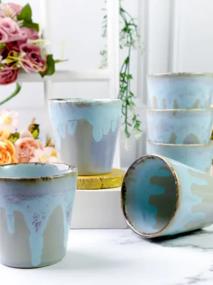 A dynamic arrangement of the ceramic tumblers, with some stacked and one lying on its side. This playful composition shows off the product from multiple angles and highlights its glossy finish.