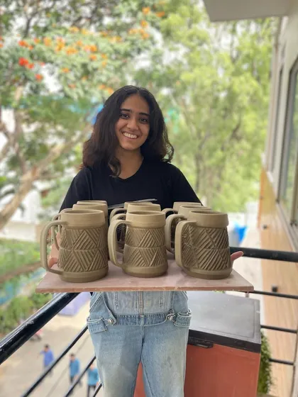 Vrinda proudly holding a tray of her hand-carved beer mugs, part of her graduation collection.