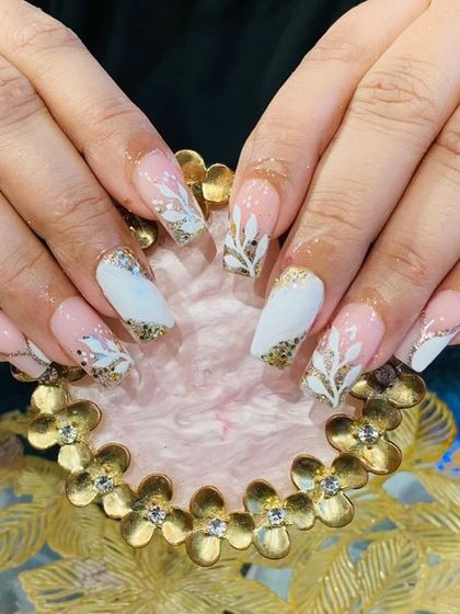An elegant white and gold design with hand-painted white leaves over a glittery gold base on square-tipped extensions.
