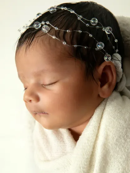 A detailed close-up of a newborn's profile, highlighting their delicate features, soft skin, and the beautiful beaded headband.