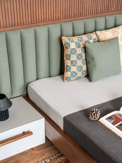Texture plays a vital role in creating a cozy bedroom. In Amber House, we paired a soft, vertically channeled headboard in sage green with patterned cushions and a simple white nightstand, creating a composition that is both tactile and visually calming.