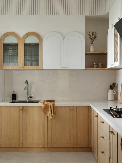 In this Japandi-style kitchen, I opted for a clean look using white oak veneer for the lower cabinets and white for the upper ones. Arched cabinet doors and fluted detailing to conceal the chimney pipe add soft, organic shapes to the minimalist design.