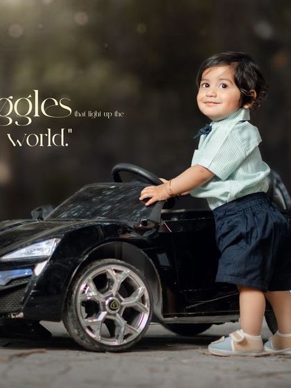 Giggles that light up the world. A little boy stands proudly next to his toy car in this charming outdoor photo.