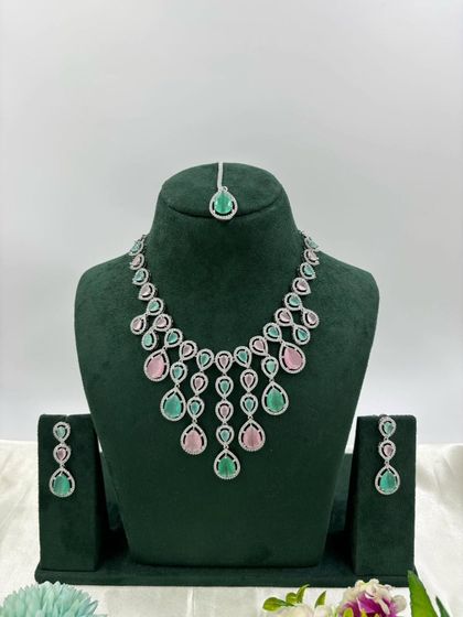An elegant AD necklace set with a matching maang tikka. The cascading design with teardrop stones is available in green, pink, and all-white, perfect for receptions and parties.