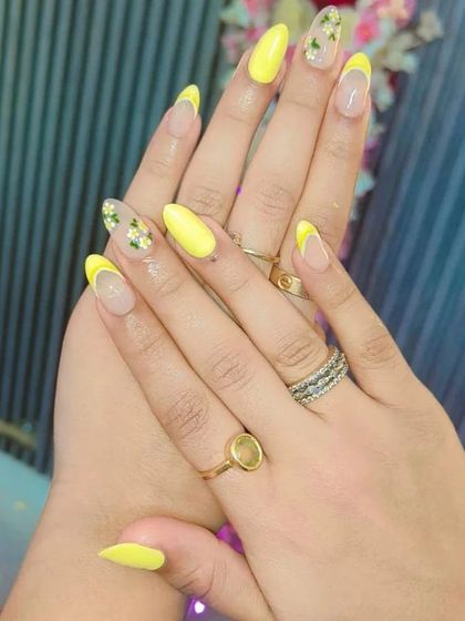 A bright yellow French manicure with accent nails featuring encapsulated dried flowers for a touch of nature.