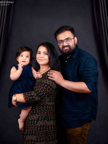 A classic family portrait with a dark, moody background. The composition draws the eye to the loving connection between the parents and their child.