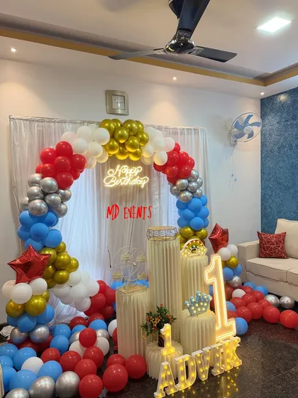 A duplicate image showing the vibrant red, blue, silver, and gold balloon arch for a first birthday party at home.