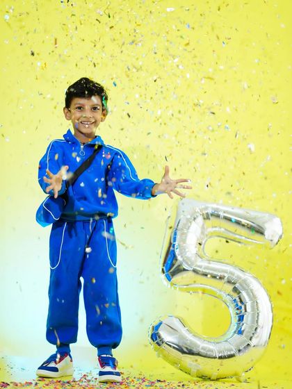 A fun shot of a five-year-old boy celebrating his birthday with confetti and a giant number '5' balloon.