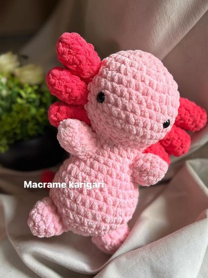 This is our pink axolotl plushie, made from soft chunky yarn. Its unique design and bright colors make it a fun and eye-catching toy.