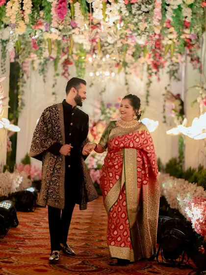 The groom leads his bride down a floral-lined aisle, their happy smiles showing the joy of their reception entrance.