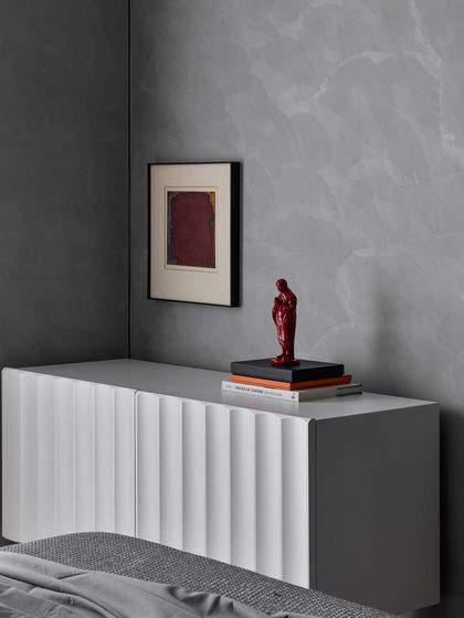 Walls of expression. A simple, fluted white console is set against a grey marble-textured wall, providing a minimalist stage for a small red sculpture and a piece of abstract art.