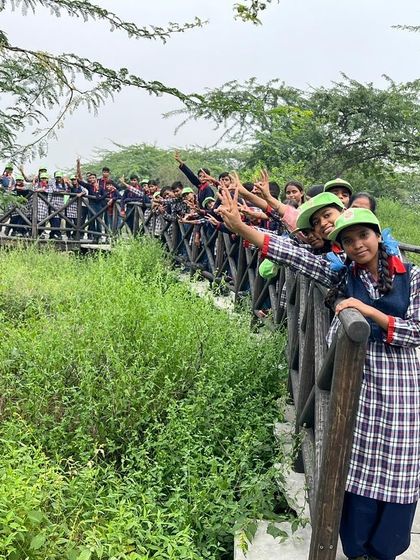 Students wave happily from a bridge at Aravali Nagar Van, enjoying the green space created through community and corporate collaboration.