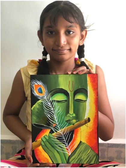 A student holds her canvas painting of Lord Krishna, created with a unique green colour palette. The white peacock feather provides a striking contrast.