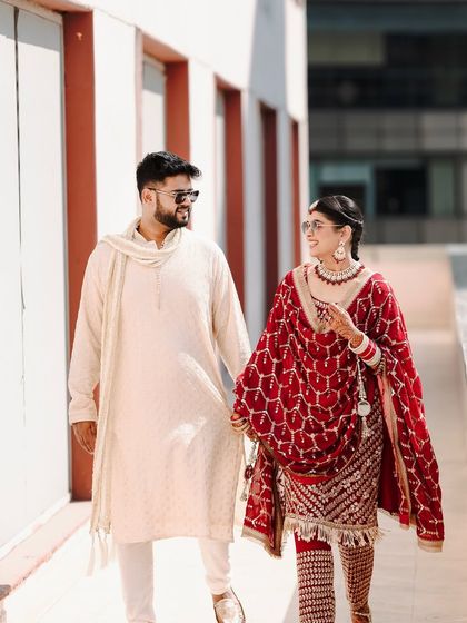 A happy walking shot of the couple, hand in hand, both wearing sunglasses. This candid photo captures their modern style and joyful connection.
