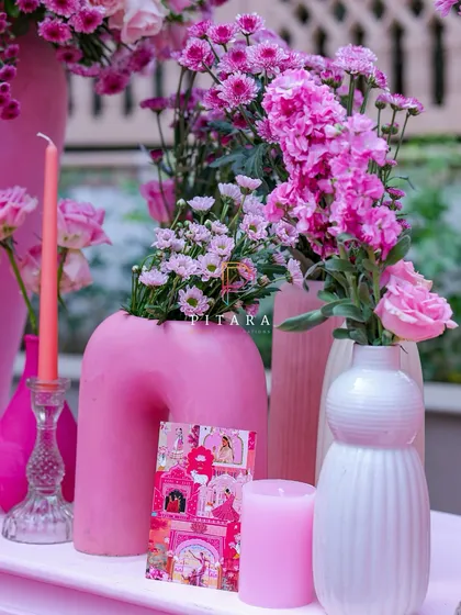 Details matter. A modern, curved matte pink vase is paired with textured white ones, taper candles, and a custom invitation card, creating a tablescape that tells a story of elegance.