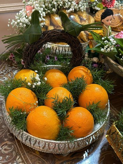 This silver platter holds fresh oranges and is decorated with a rustic twig wreath and birds made from coconut leaves. It's a unique and natural design for any event.