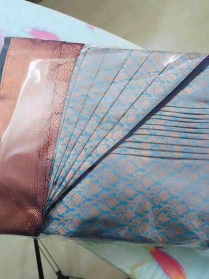 A close-up of the packed light blue saree, showing the neatness of the box fold through the transparent cover.