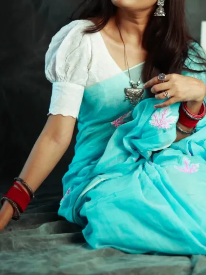 A detail shot focusing on the fabric and accessories of this beautiful light blue saree. The red bangles provide a lovely contrast, and the pose is soft and graceful.