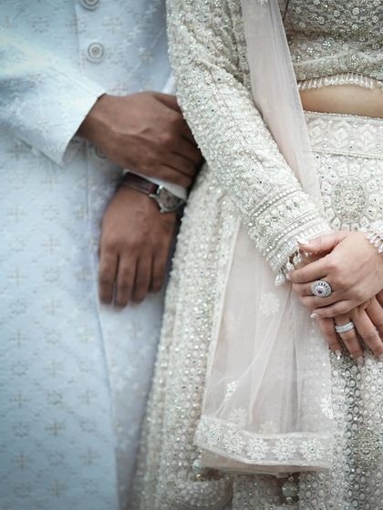 A detail shot of a couple in elegant white attire, showcasing the texture of their outfits and their gentle hold. This highlights the sophisticated details of a modern wedding.