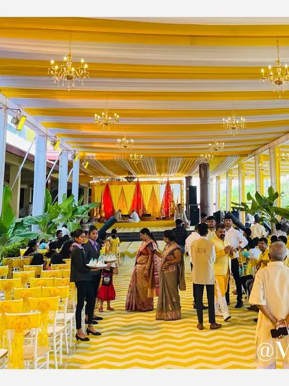 The vibrant atmosphere of a Haldi ceremony in full swing. The yellow and white draped ceiling with chandeliers adds a touch of grandeur to the traditional event.