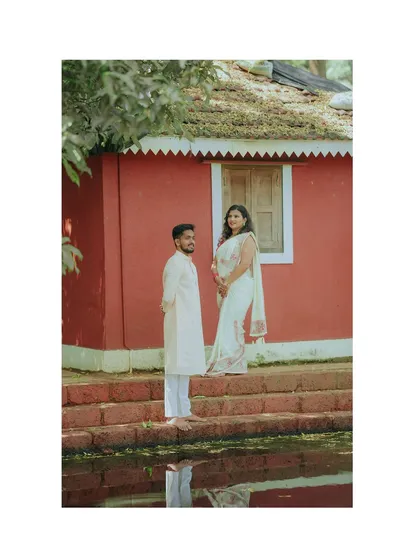 A simple, elegant portrait against a rustic red wall. The couple's traditional white outfits create a beautiful contrast in this serene pre-wedding photo.