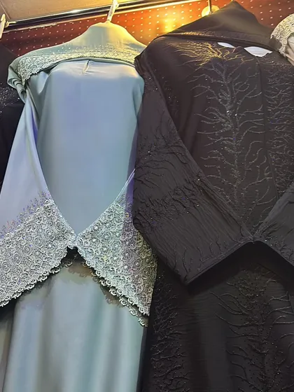 A closer view of a light blue abaya with a delicate lace overlay and a black abaya with textured, embossed patterns.