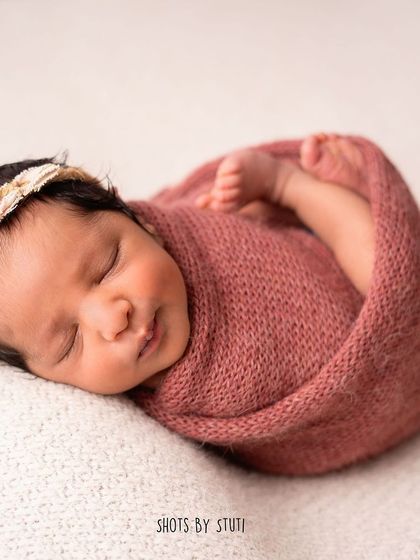 A close-up of a perfectly swaddled newborn. The swaddle helps keep babies calm and sleepy, allowing for these peaceful and classic poses.
