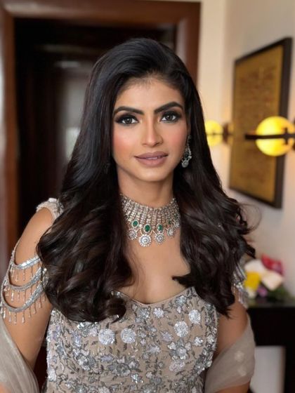 A straight-on shot showing the beautiful symmetry of the makeup. The nude lipstick and defined brows balance the glamorous eye makeup and heavy jewelry perfectly.