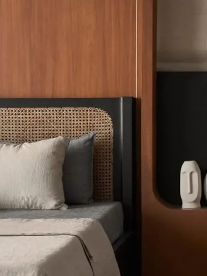 The custom black bed with its two-tone cushion and rattan headboard is the centerpiece of this bedroom. The design is a study in contrasts, balancing dark tones with natural textures.