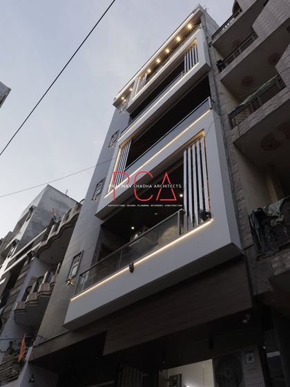 A daytime view looking up at 'The Cursive Abode'. This shot captures the vertical metal louvers and the crisp white frames that add a layer of detail and sophistication to the facade.