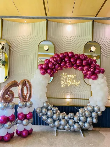 A chic 60th birthday setup with a circular balloon arch in magenta, white, and silver. The rose gold '60' balloon numbers add a trendy touch.