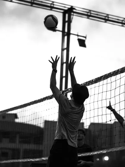 A player setting the ball against the evening sky, a beautiful black and white shot of volleyball in its purest form.