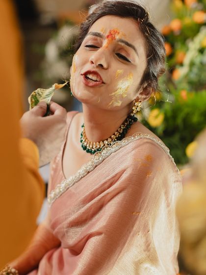 A playful moment during the Haldi ceremony, where the bride is lovingly smeared with turmeric paste. Her expression is a perfect mix of joy and mischief.