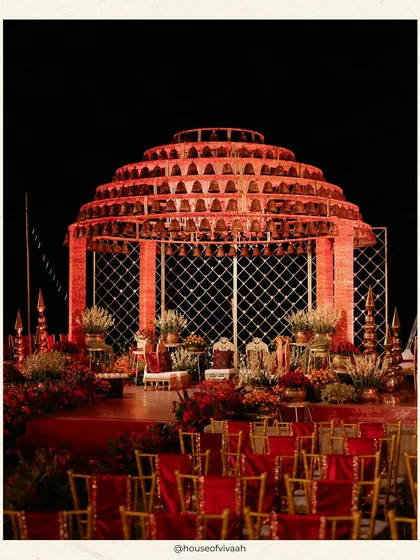 The stunning bell mandap glows against the night sky, its architectural form and warm lighting creating a powerful and dramatic centerpiece for the wedding ceremony.