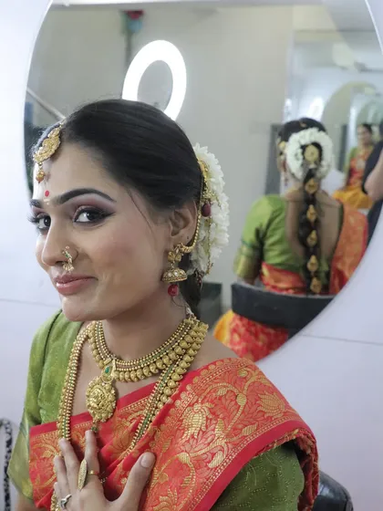 A candid mirror shot of the model, showing her happiness with the final look. The reflection also gives a glimpse of the traditional braided hairstyle adorned with flowers.