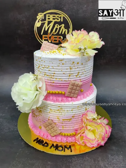 Because the best mom deserves the best cake. This two-tier design in pink and white features delicate line texturing, edible chocolate bars, and beautiful flowers, all for a special mother's birthday.