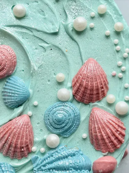 A close-up of the mermaid-themed cake, showing the shimmering, edible fondant shells in pink and blue, scattered with pearls.