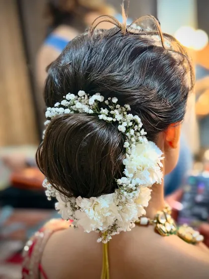 A complete bridal look includes a perfect hairstyle. I work closely with talented hairstylists to create beautiful updos, like this intricate floral bun, that complement both the makeup and the outfit.