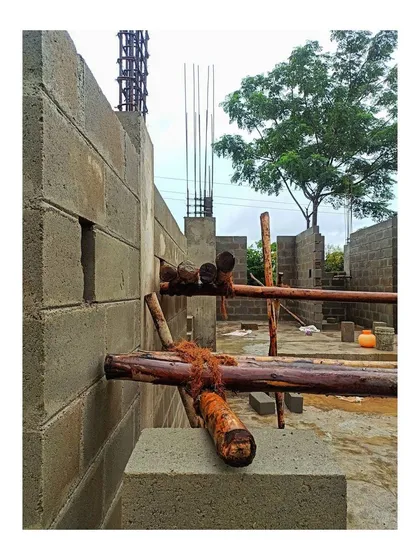 A close-up view from the construction site in Mysore, showing the concrete block masonry and temporary wooden scaffolding. This perspective highlights the textures and raw materials that form the structure, showcasing the tangible process of turning blueprints into a physical building.