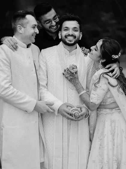 A candid black and white photo of a groom surrounded by his loved ones. The spontaneous smiles and affectionate gestures create a lively and heartfelt group portrait.