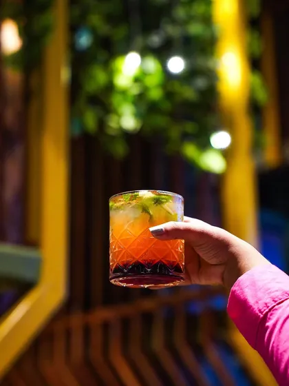 A hand holds a layered orange and red cocktail against a softly blurred background of a bar. This simple, elegant shot focuses on the drink and creates a relaxed, social atmosphere.