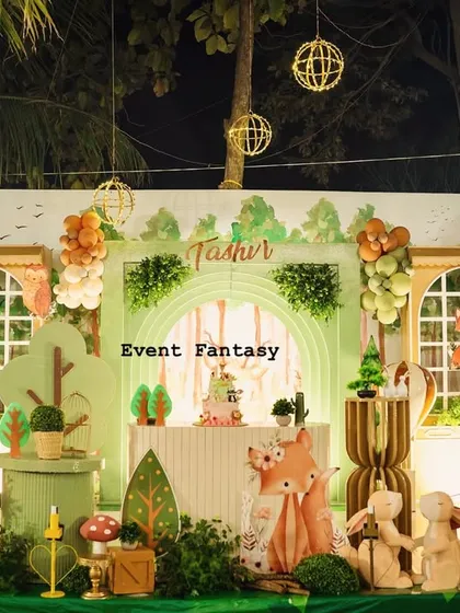 Tashvi's woodland birthday stage glowing in the evening light. The setup features a cozy house backdrop, illuminated by string lights, with cute fox and rabbit props creating a warm and inviting atmosphere.