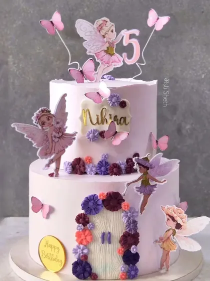 A two-tiered fairy and butterfly cake for a 5th birthday. This grander version features a fairy door and multiple fairy toppers for an enchanting look.