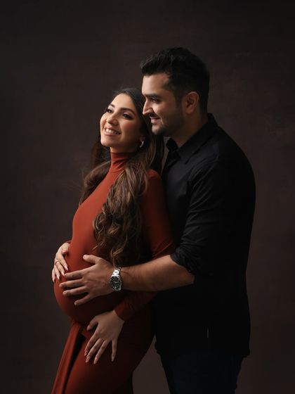 A beautiful portrait of a couple's love. His gentle embrace from behind as she glows in a stunning rust-colored gown creates a warm and intimate moment.