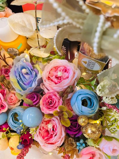 A close up of a stunning floral birthday hamper, overflowing with colorful artificial flowers, skincare items, and Ferrero Rocher. It's a true feast for the eyes.