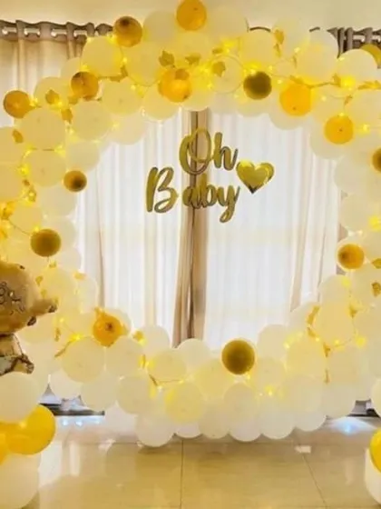 A simple and sweet 'Oh Baby' shower with a circular balloon arch in white and yellow, illuminated by fairy lights.