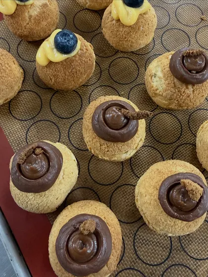 A close-up of our choux pastries, showing the different fillings. We offer a variety, including chocolate, blueberry, and lemon curd, each with a crispy craquelin top.