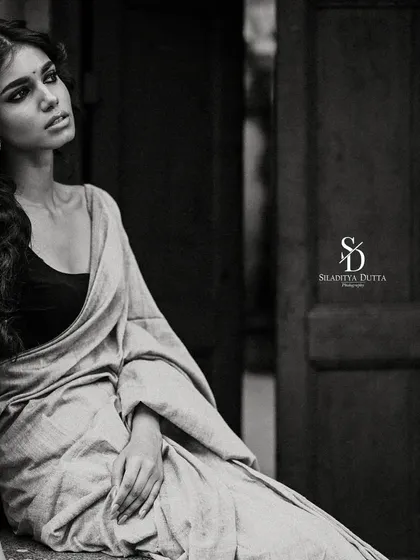 A soulful black and white portrait of a model sitting in a rustic doorway. The deep shadows and her melancholic expression give the image a cinematic and timeless quality.