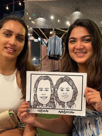 Two friends posing with their fun caricature at an event in BKC.