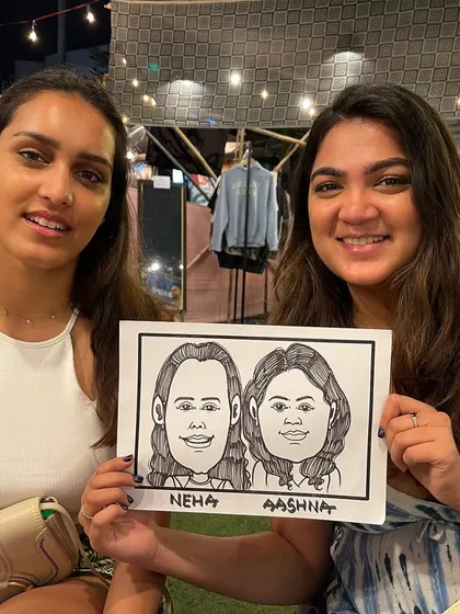 Two friends posing with their fun caricature at an event in BKC.